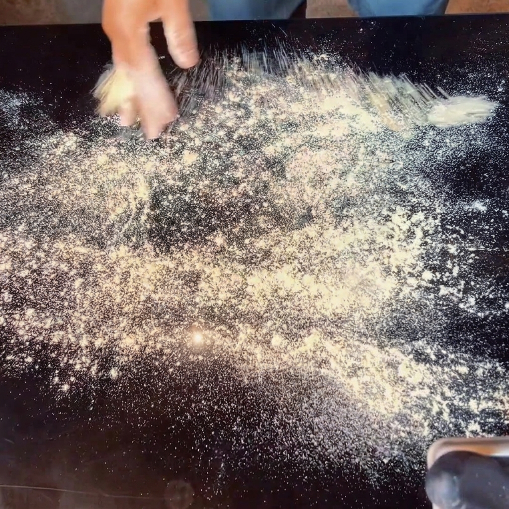 Manos estirando masa de pizza sobre una superficie enharinada.