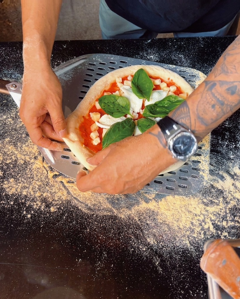 Primer plano de hojas de albahaca fresca siendo colocadas sobre la pizza preparada.