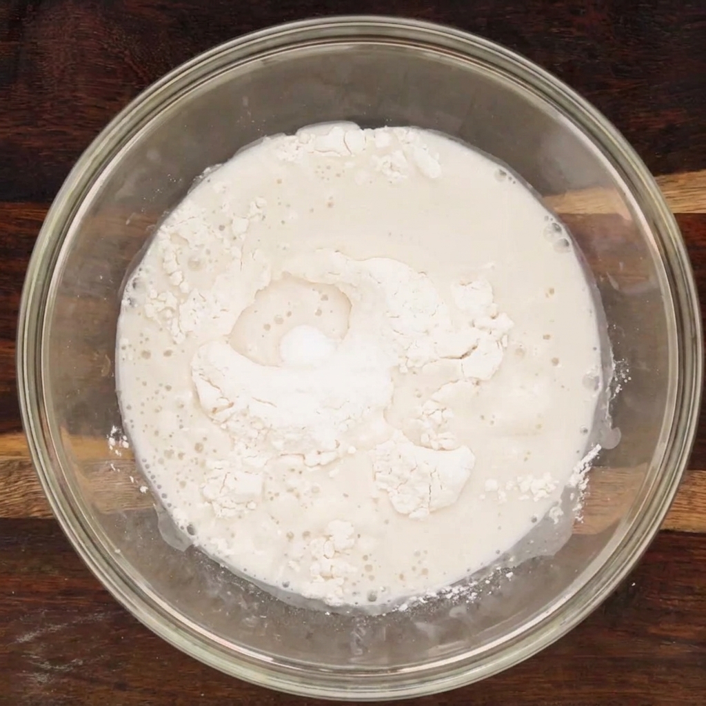 Ingredientes líquidos y secos combinados en un tazón de vidrio, formando una masa rústica.