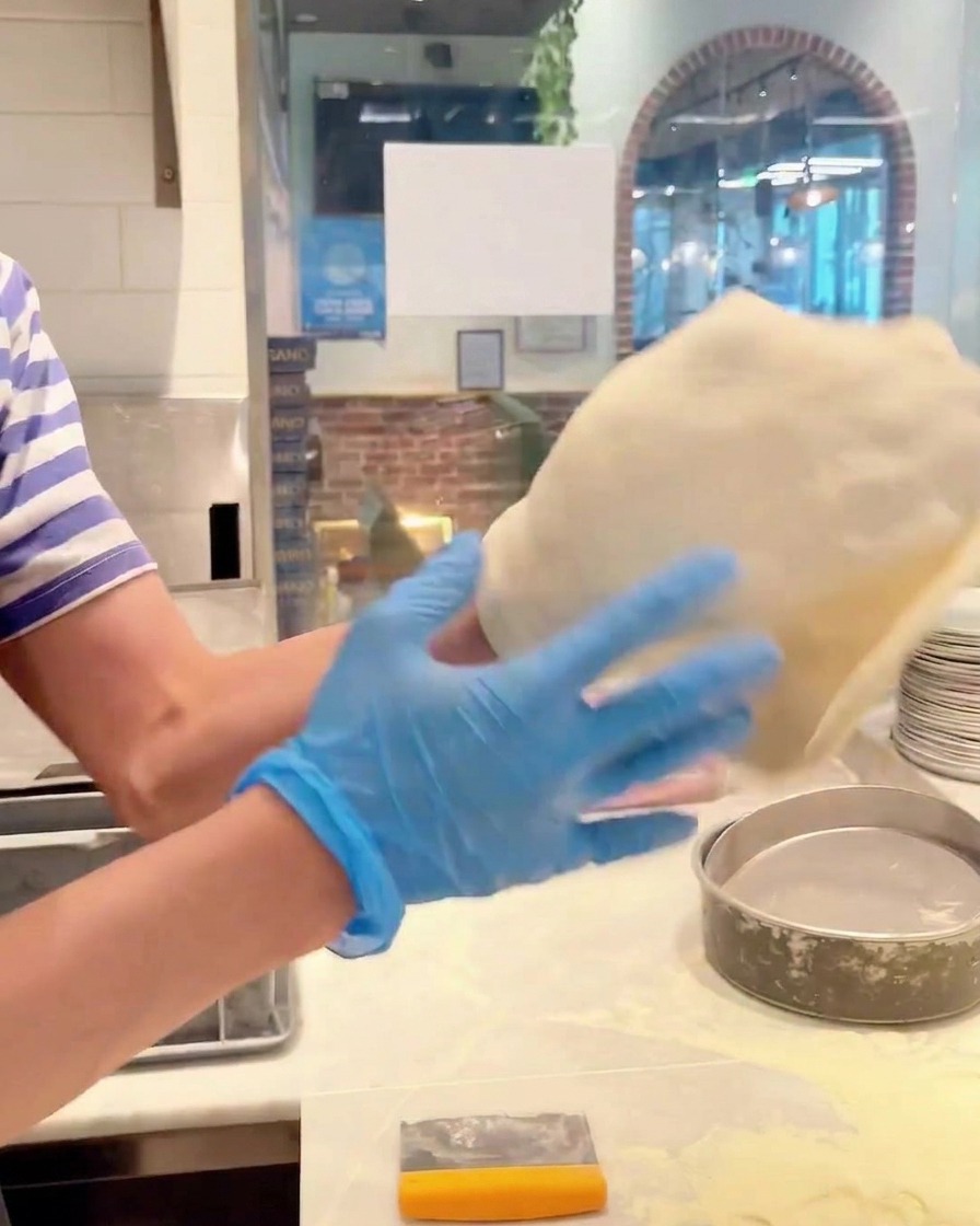 Manos rotando una pieza de masa de pizza para estirarla en un círculo más grande.