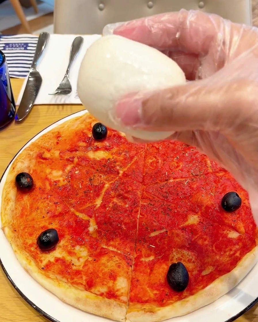 Trozos de mozzarella de búfala fresca siendo colocados sobre la pizza.
