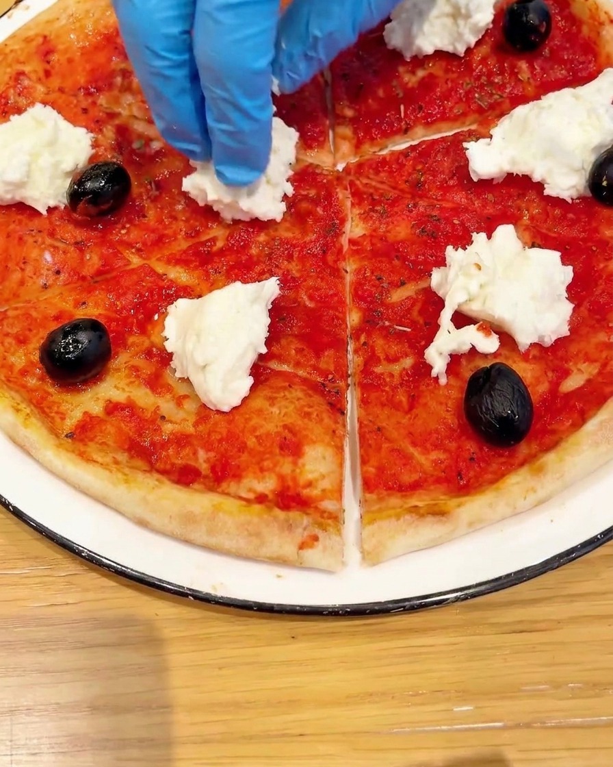 Vista superior de una base de pizza decorada con mitades de tomate cherry y hojas de albahaca verde.