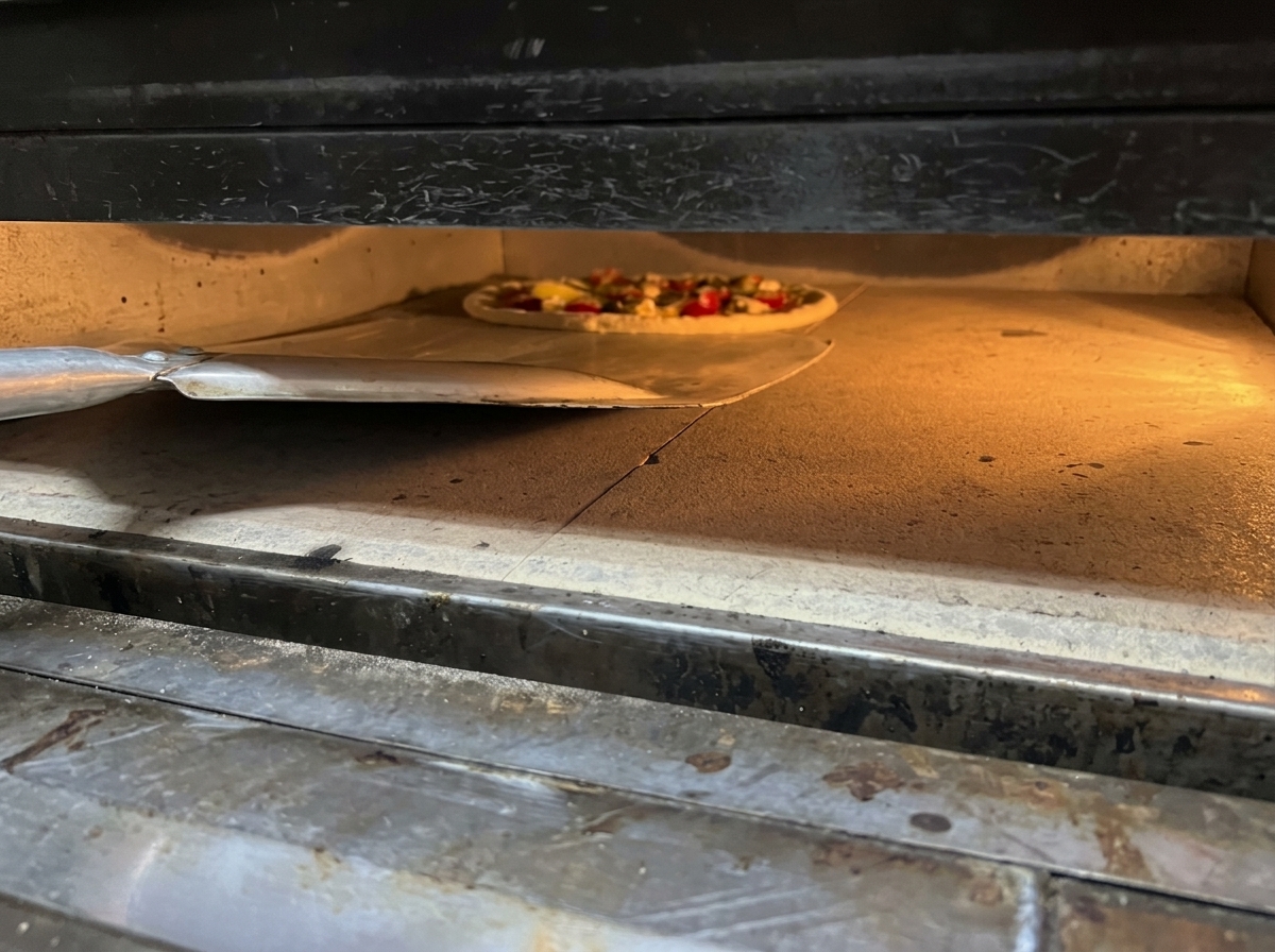 Deslizando una pizza fresca desde una pala de metal hacia un horno muy caliente sobre una piedra de horneado.