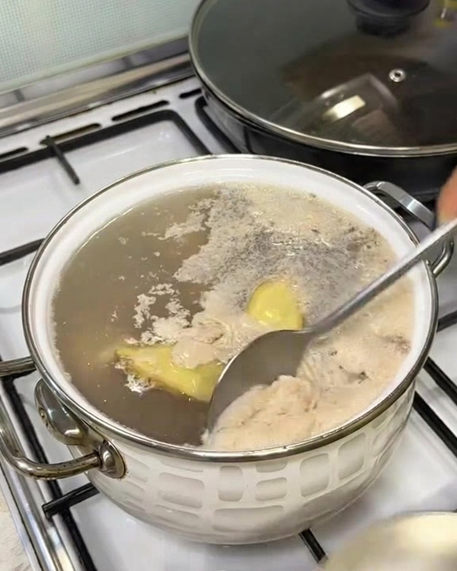 Una cuchara retirando la espuma grisácea de la superficie del agua hirviendo en una olla.