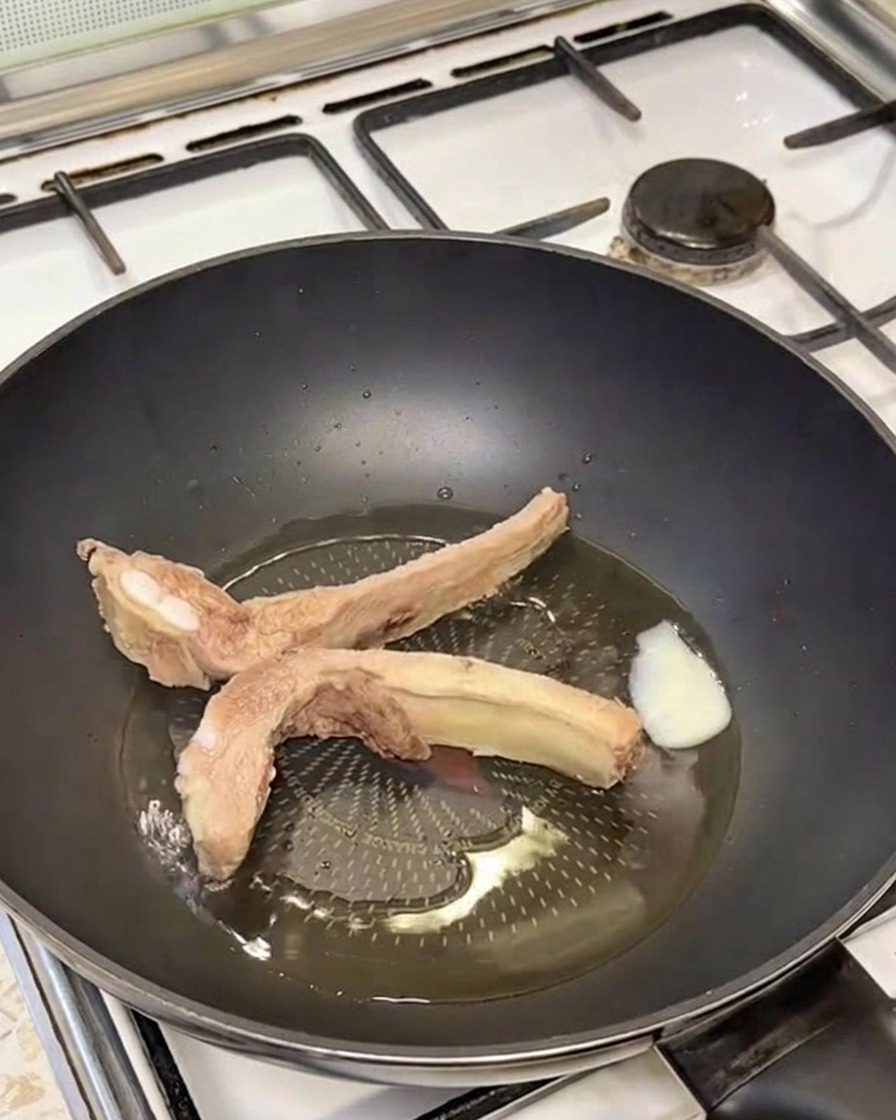 Costillas de cerdo selladas de color dorado chisporroteando en una sartén con manteca derretida.