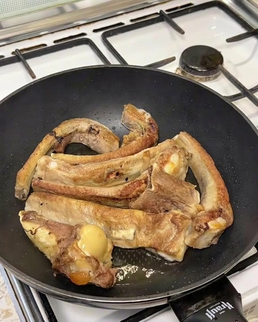 Agua hirviendo vertida sobre las costillas selladas en una sartén, creando una nube de vapor.