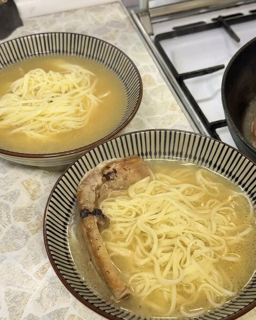 Primer plano de una costilla de cerdo braseada, tierna y dorada, colocándose en un tazón de ramen.