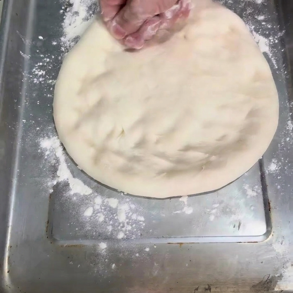 La masa siendo aplanada en forma circular sobre una bandeja para hornear.