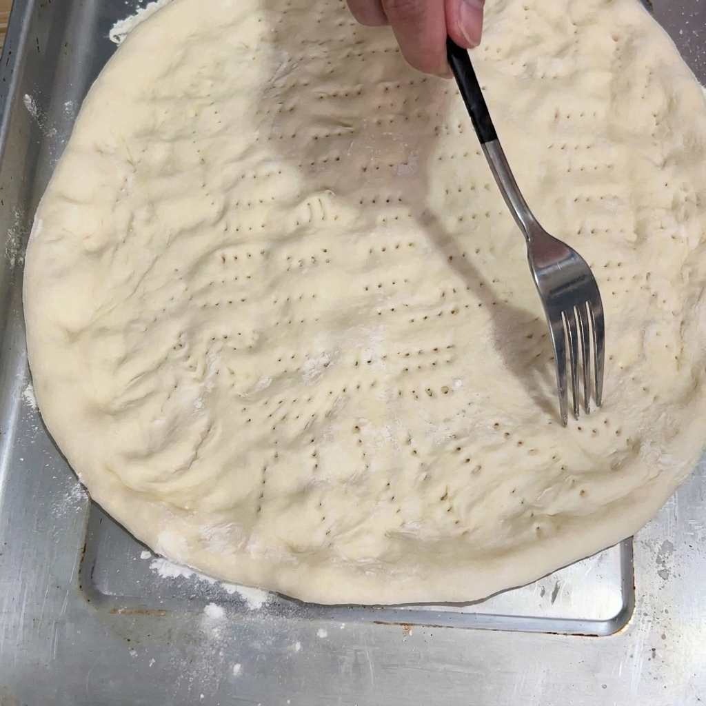 Un tenedor pinchando la base de masa aplanada en la bandeja para hornear.
