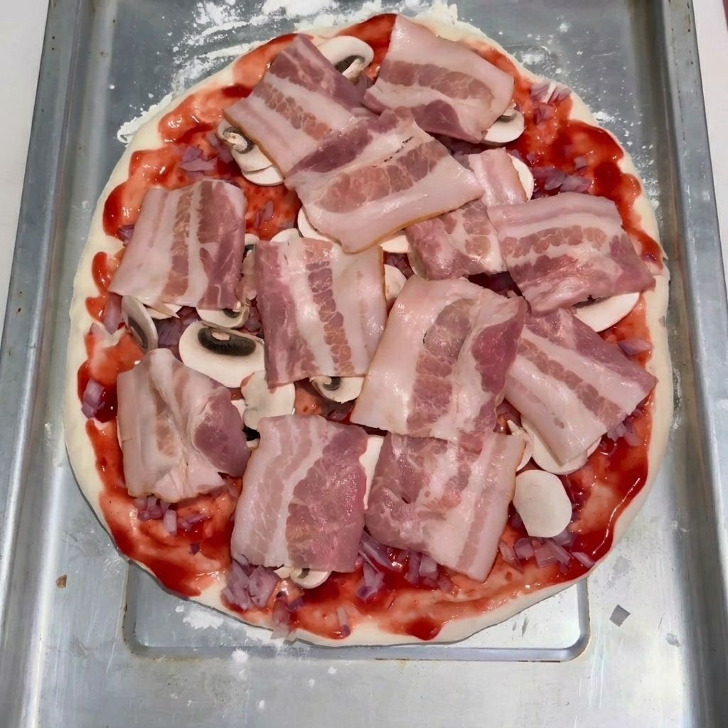 Lonchas de bacon crudo dispuestas ordenadamente sobre una capa de champiñones laminados y salsa de tomate en una base de masa de pizza aplanada.