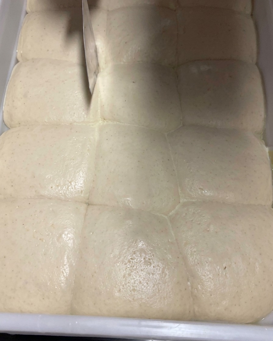Primer plano de masa fermentada siendo dividida cuidadosamente en porciones con un cortador de metal.