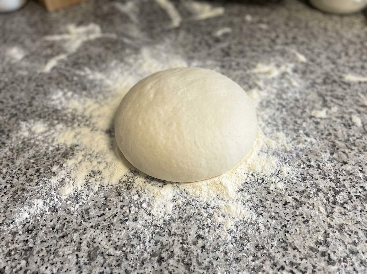 Masa siendo presionada y moldeada en un círculo sobre una superficie enharinada.