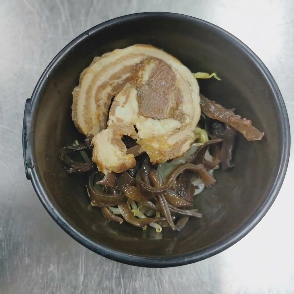 Un primer plano de un tazón para servir que contiene carne de cerdo chashu y setas oreja de madera listos para emplatar.