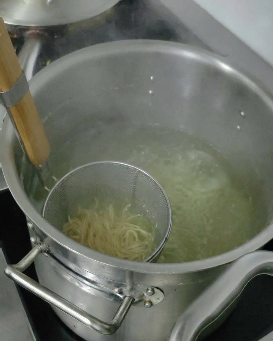 Fideos ramen cocidos siendo levantados en un colador para escurrir el exceso de agua antes de añadirlos al tazón.