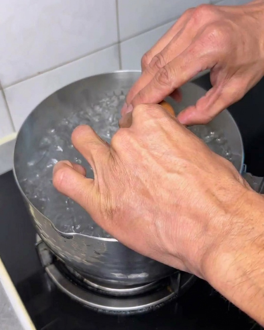 Un huevo crudo siendo echado en agua hirviendo.