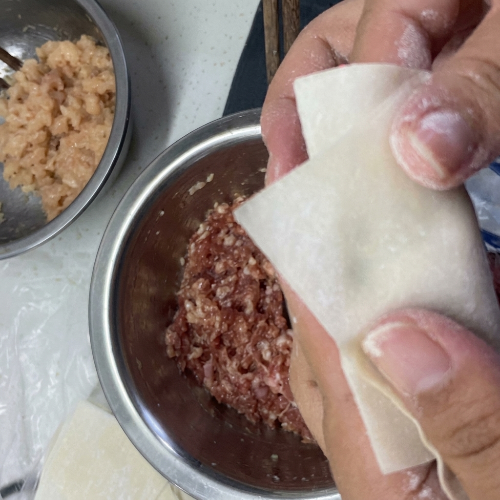 Manos doblando un envoltorio de wonton alrededor del relleno y sellando los bordes con agua.