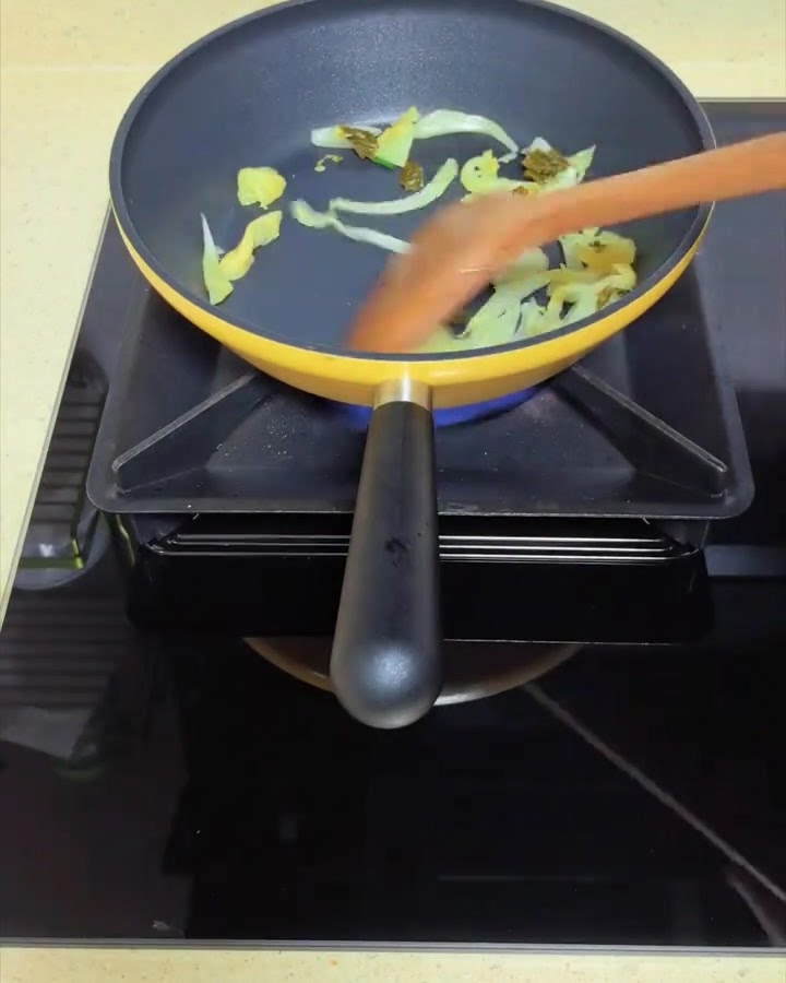 Hojas de mostaza encurtidas salteándose en una sartén amarilla con una espátula de madera.