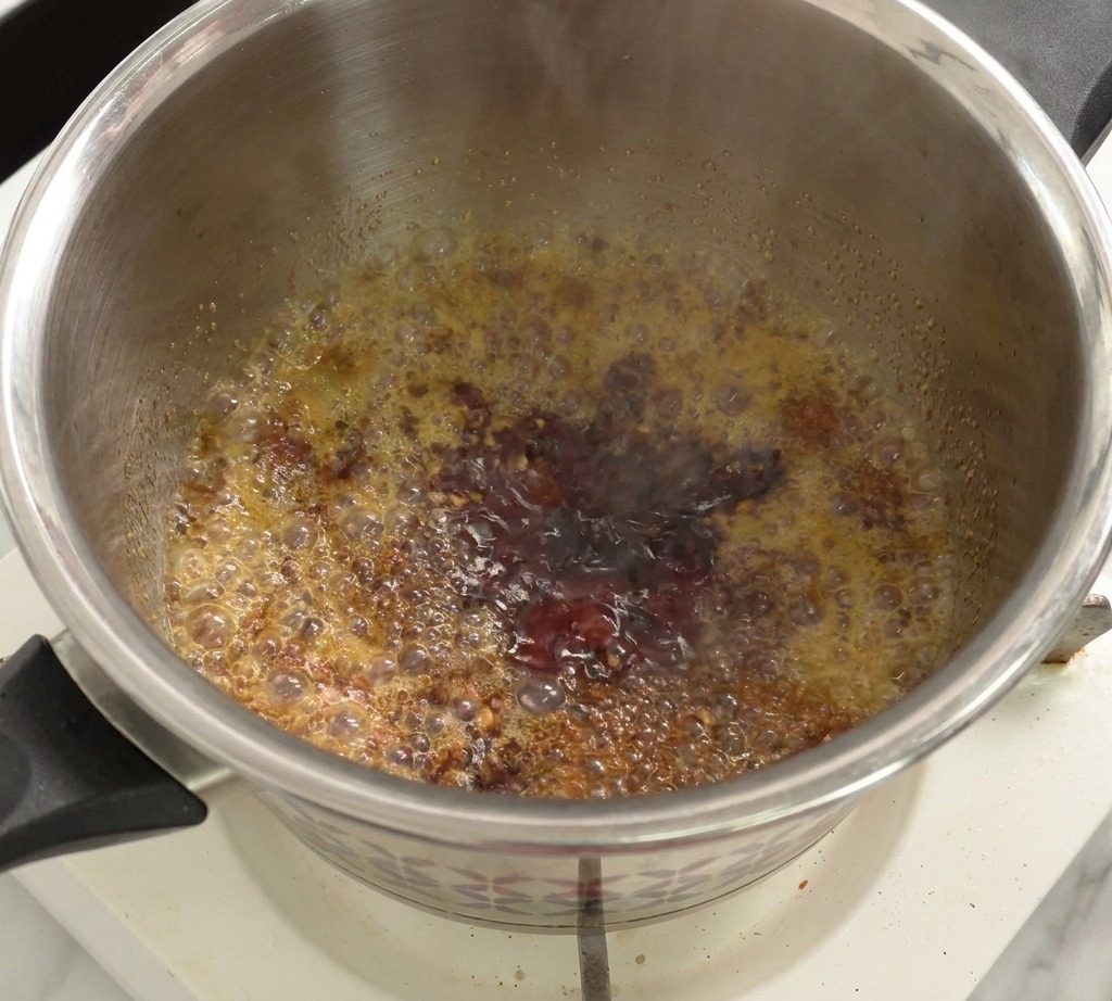 Una mezcla de salsa de tomate y vinagre hirviendo a fuego lento y burbujeando en una olla.