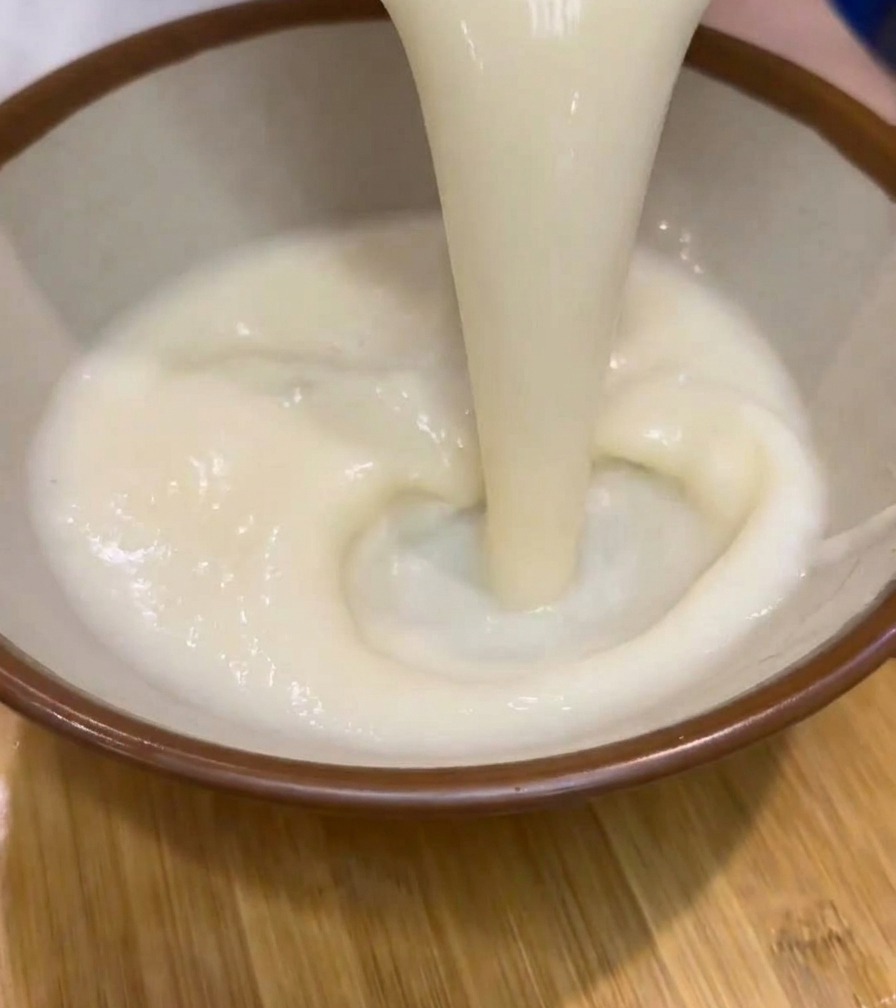 Sopa de ramen blanca, espesa y cremosa siendo vertida desde una jarra a un cuenco de cerámica con borde marrón.