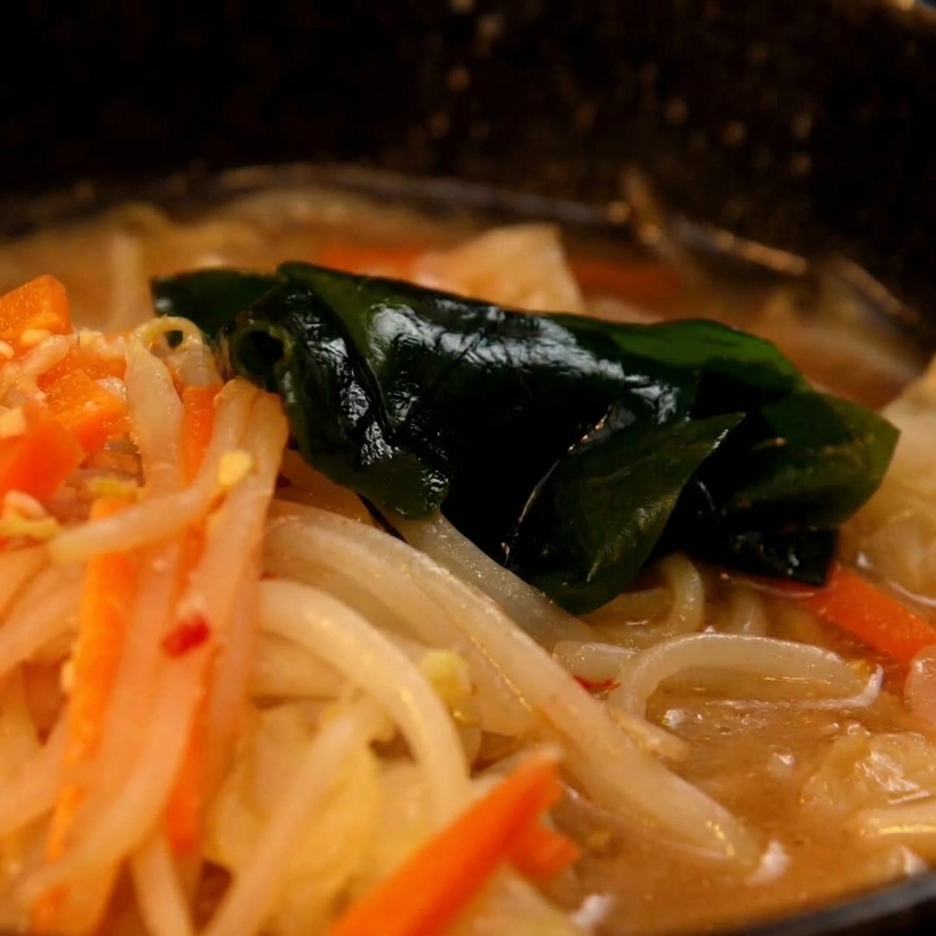 Fideos de ramen cocidos siendo trasladados desde una olla al tazón con la base de sopa de miso.