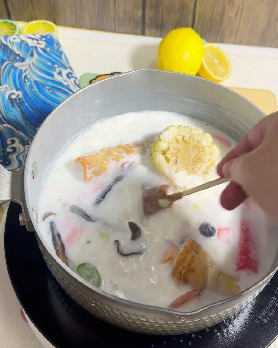 Fideos de ramen siendo añadidos a la olla con el caldo cremoso y los ingredientes cocidos.