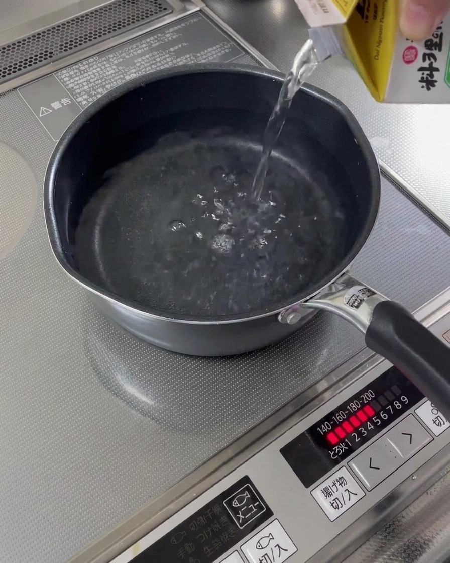 Agua vertiéndose desde un cartón en un cazo sobre la cocina.