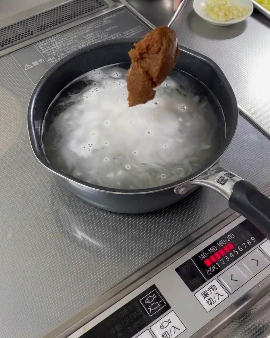 Una cucharada de pasta de miso siendo añadida a una olla de caldo hirviendo.
