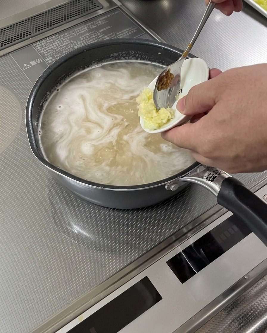 Ajo y jengibre rallados siendo añadidos a una base de sopa hirviendo.