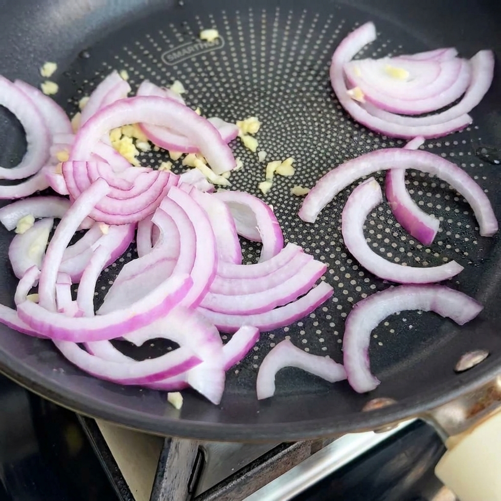 Cebollas y ajo salteándose en una sartén, liberando su aroma.