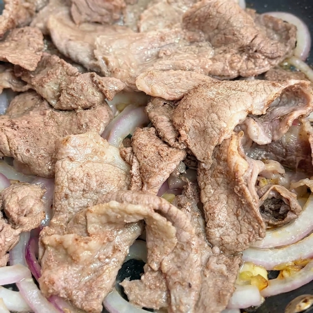Salsa oscura teriyaki siendo vertida en una sartén sobre las rodajas de carne y cebolla.