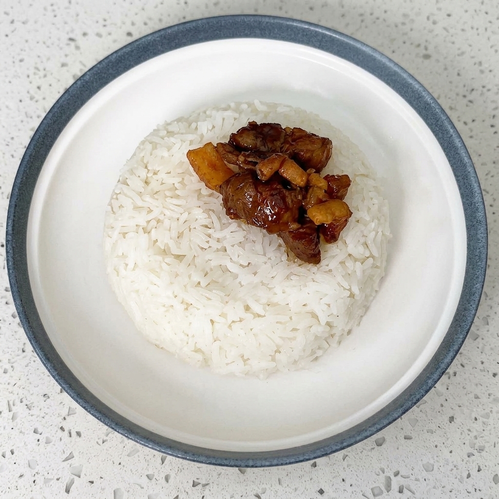 Jugosas rodajas de carne colocadas con palillos sobre un tazón de arroz blanco.
