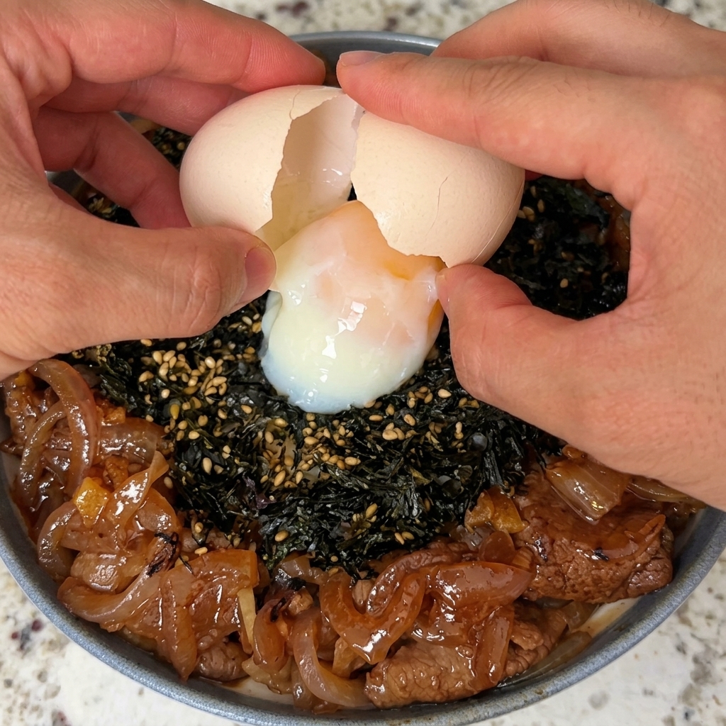 Un huevo onsen partido con cuidado y colocado sobre un tazón de arroz con carne y algas.