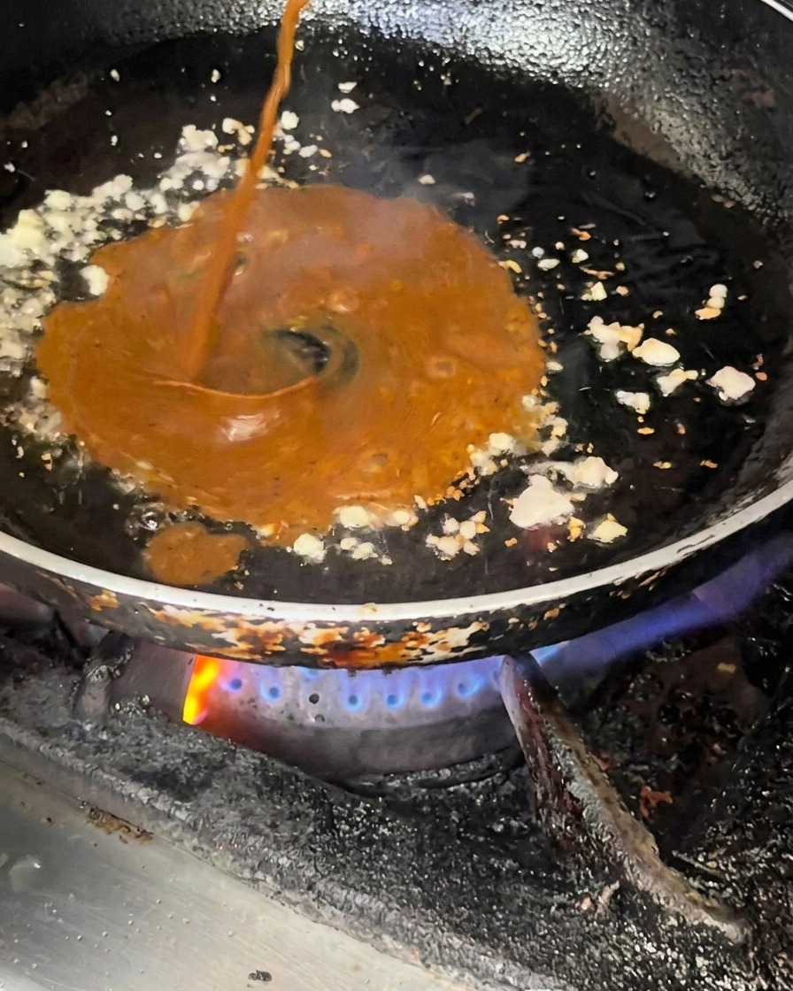 Salsa oscura vertiéndose sobre la sartén con el sofrito.