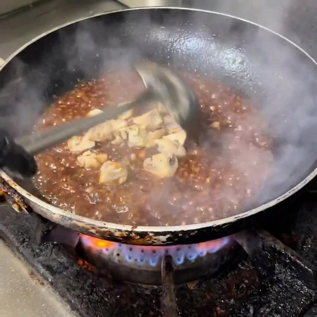 Champiñones troceados cocinándose en una salsa brillante en la sartén.