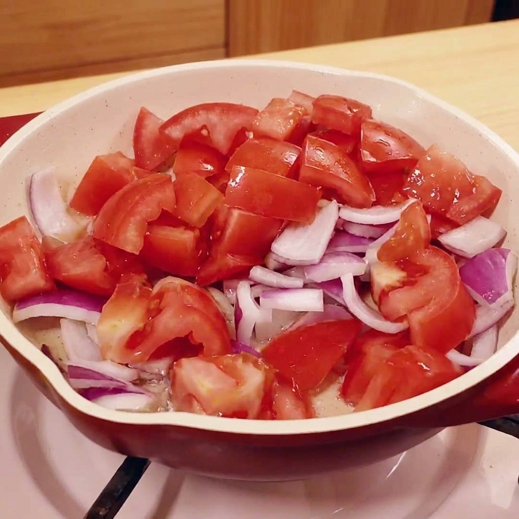 Tomates troceados y cebolla morada cocinándose en una sartén.