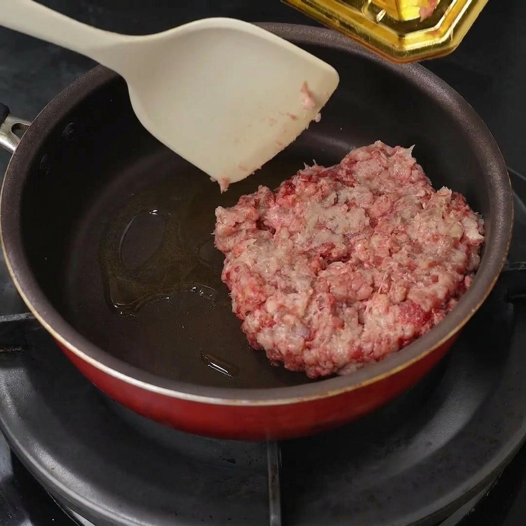 Carne picada cruda colocada en una sartén con aceite, separada con una espátula.