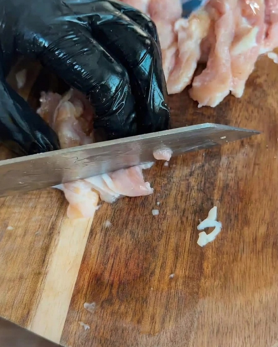 Trozos de pollo crudo picado dispuestos sobre una tabla de cortar de madera.