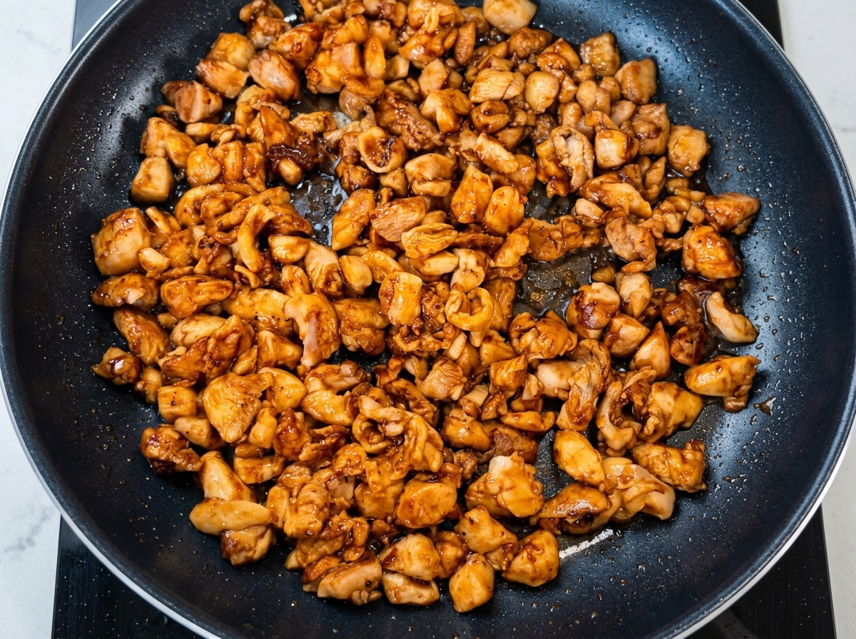 Cebollino picado siendo añadido a la sartén con el pollo dorado.