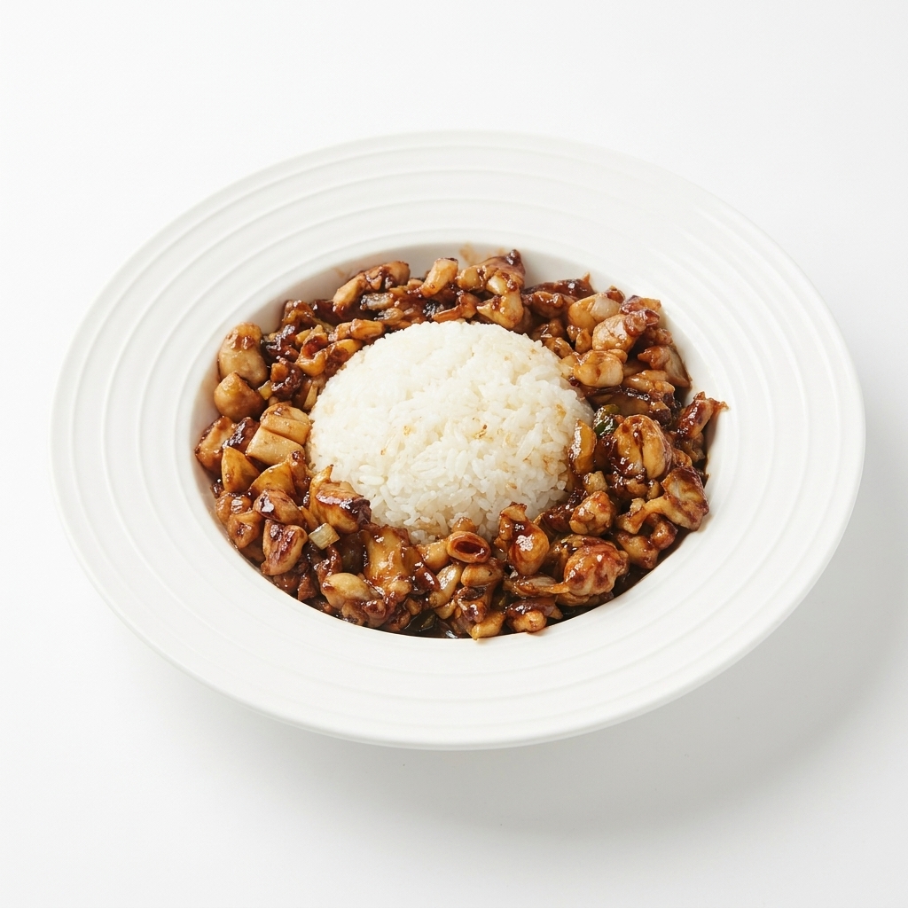 Salteado de pollo glaseado siendo dispuesto alrededor del montículo de arroz en un plato blanco.
