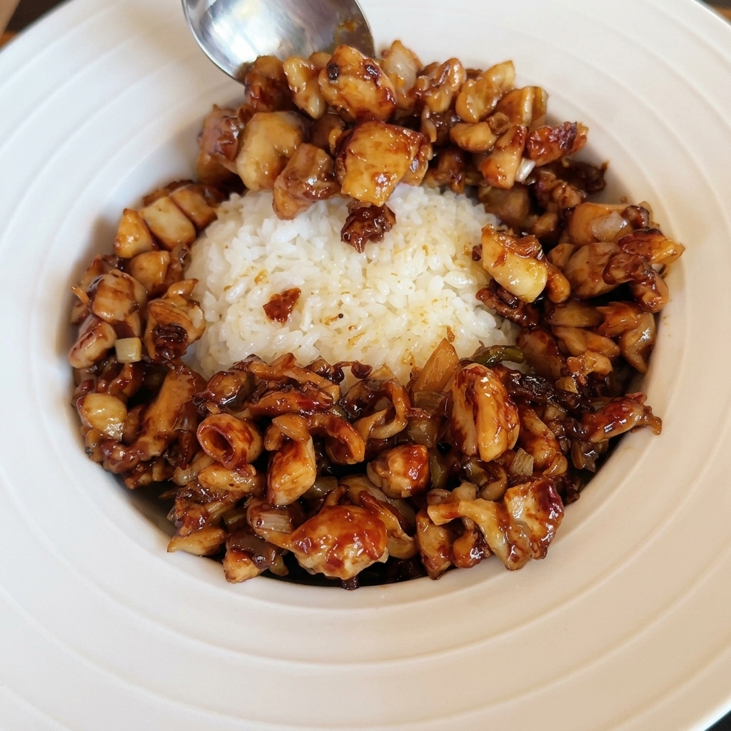 Un huevo frito perfectamente hecho siendo colocado sobre un tazón de arroz y pollo salteado.