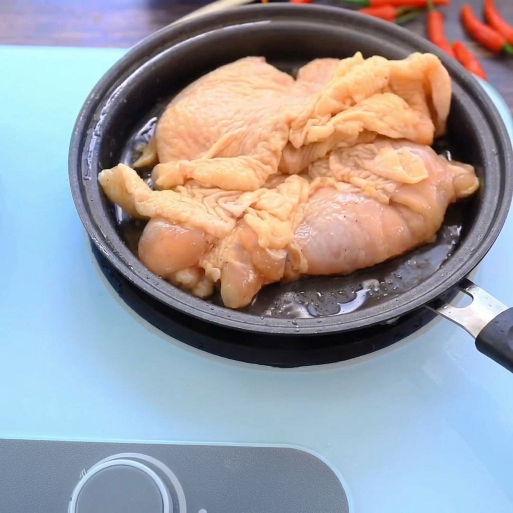 Muslos de pollo dorándose en una sartén caliente, mostrando una superficie dorada y crujiente.