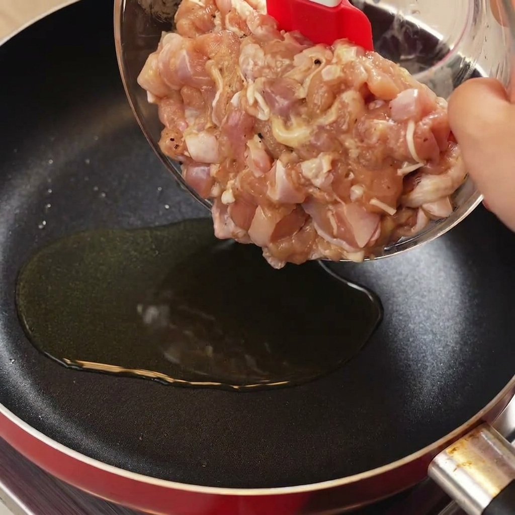 Usando una espátula roja para pasar pollo crudo marinado a una sartén caliente con aceite.