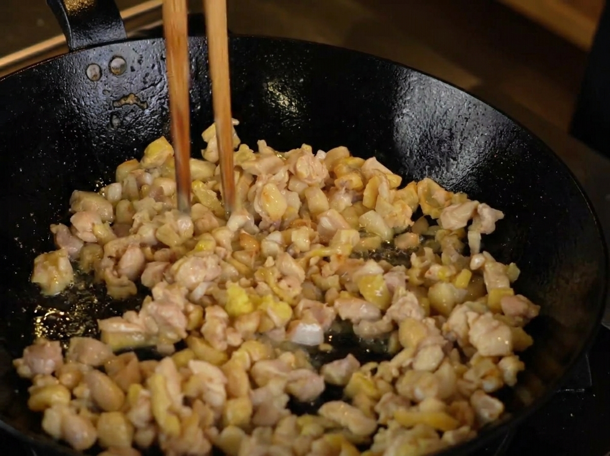 Jengibre rallado siendo añadido al pollo que se dora en la sartén.