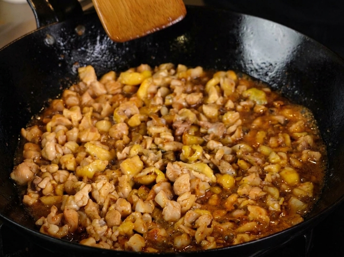 Pollo en salsa oscura cocinándose con pimienta negra, siendo removido con una espátula de madera.