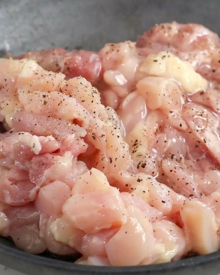 Pollo crudo picado en un bol cubierto con pimienta negra y condimentos líquidos.