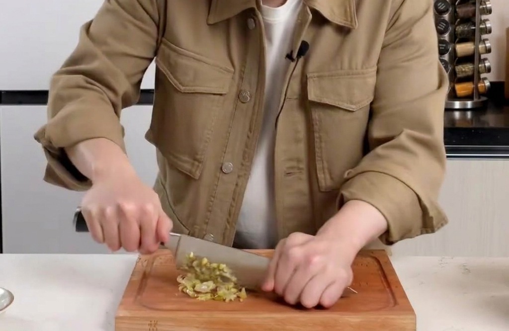 Picando finamente hojas de mostaza encurtidas en una tabla de madera con un cuchillo.