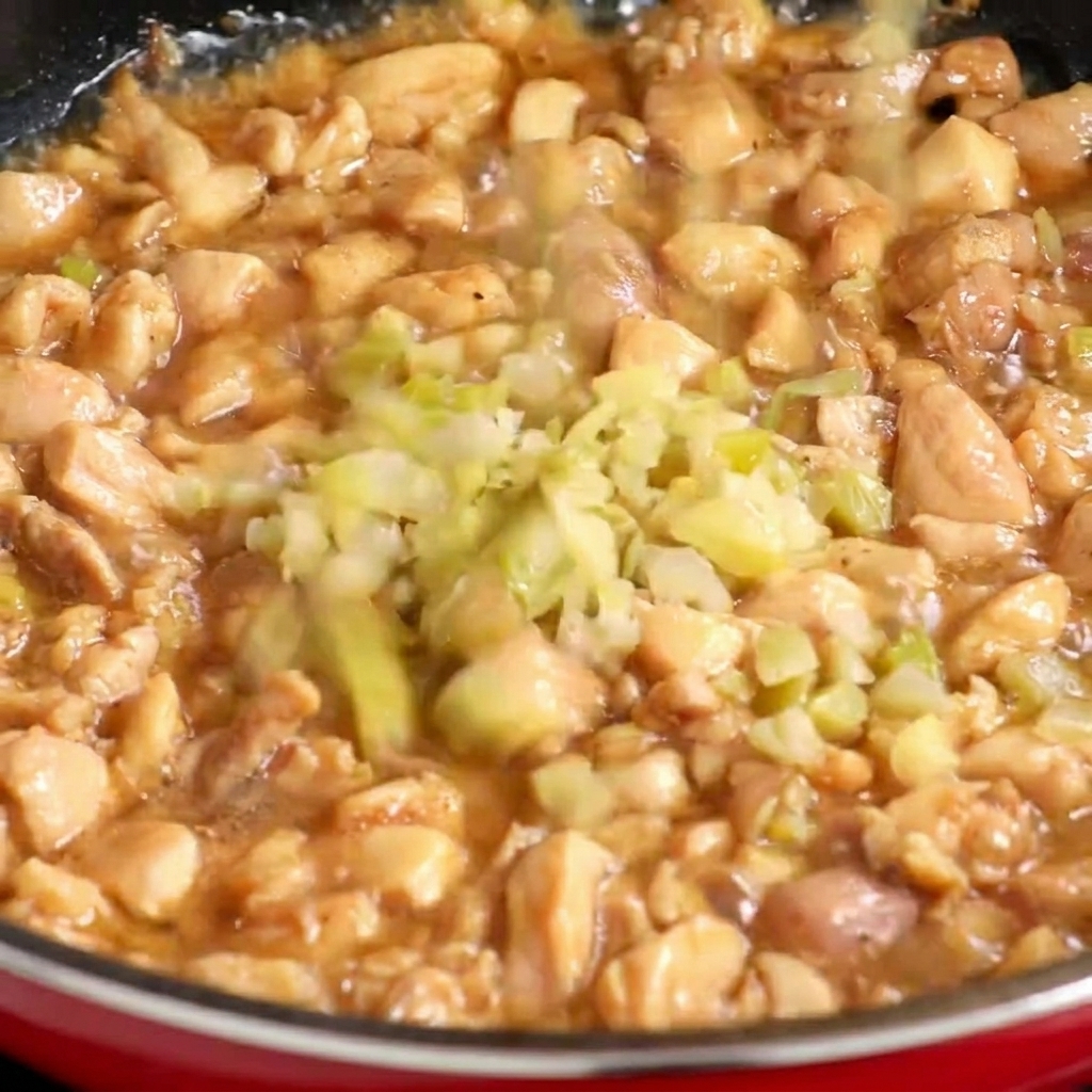 Hojas de mostaza encurtidas cortadas en cubitos finos que se añaden a una sartén con trozos de pollo parcialmente cocidos.