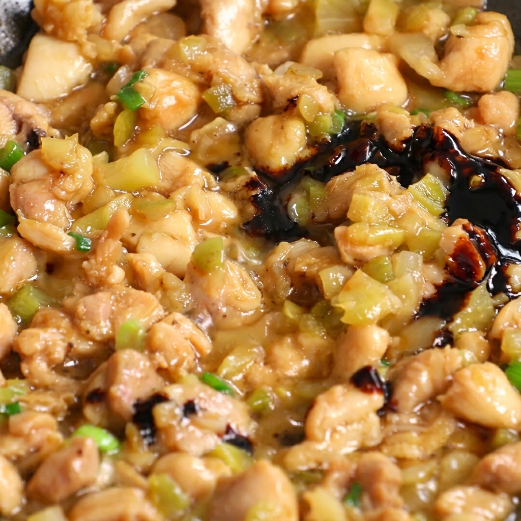 Salsa de soja oscura vertida en una sartén con la mezcla de pollo y verduras salteadas.