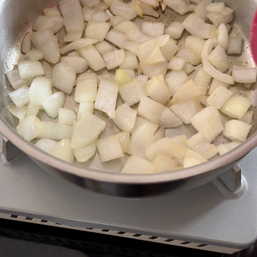 Cebollas blancas picadas siendo salteadas en una olla de metal con una espátula roja.
