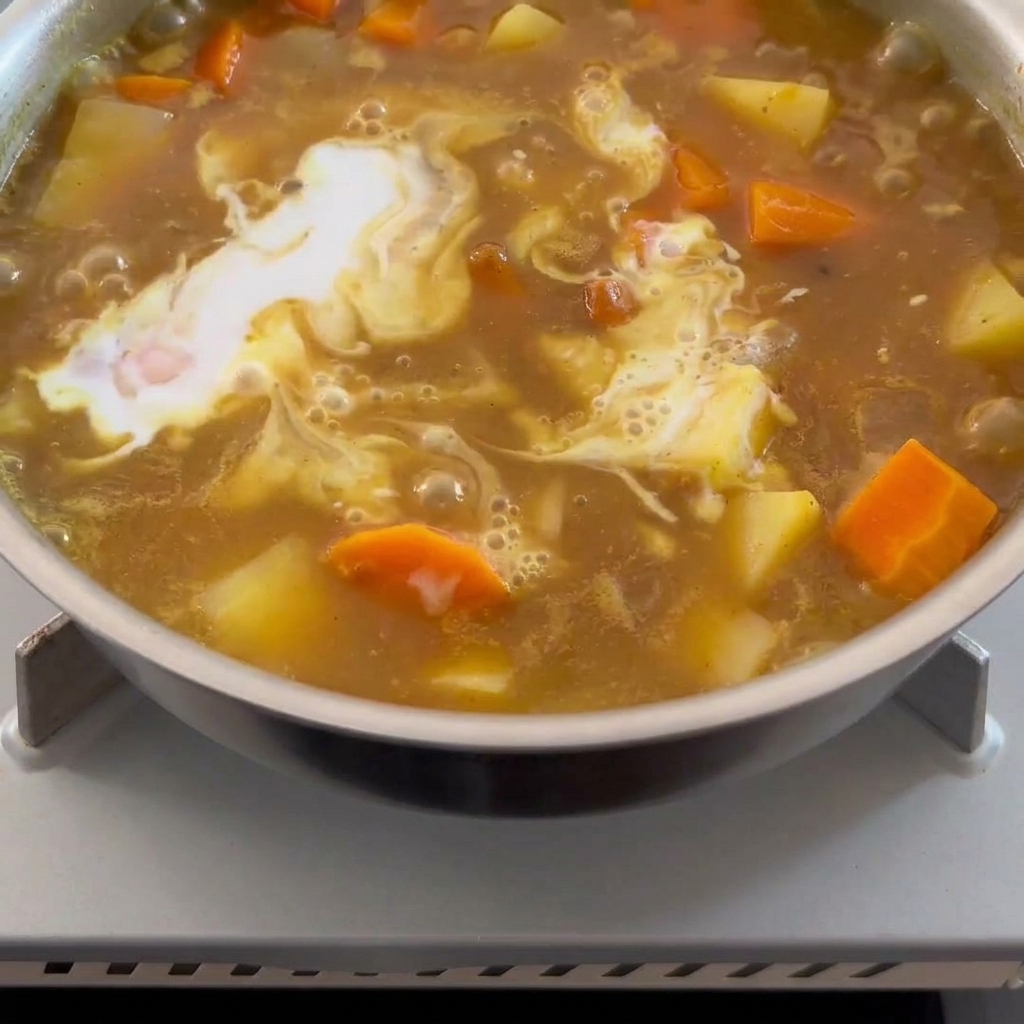Leche de coco cremosa siendo vertida en una salsa de curry marrón burbujeante.